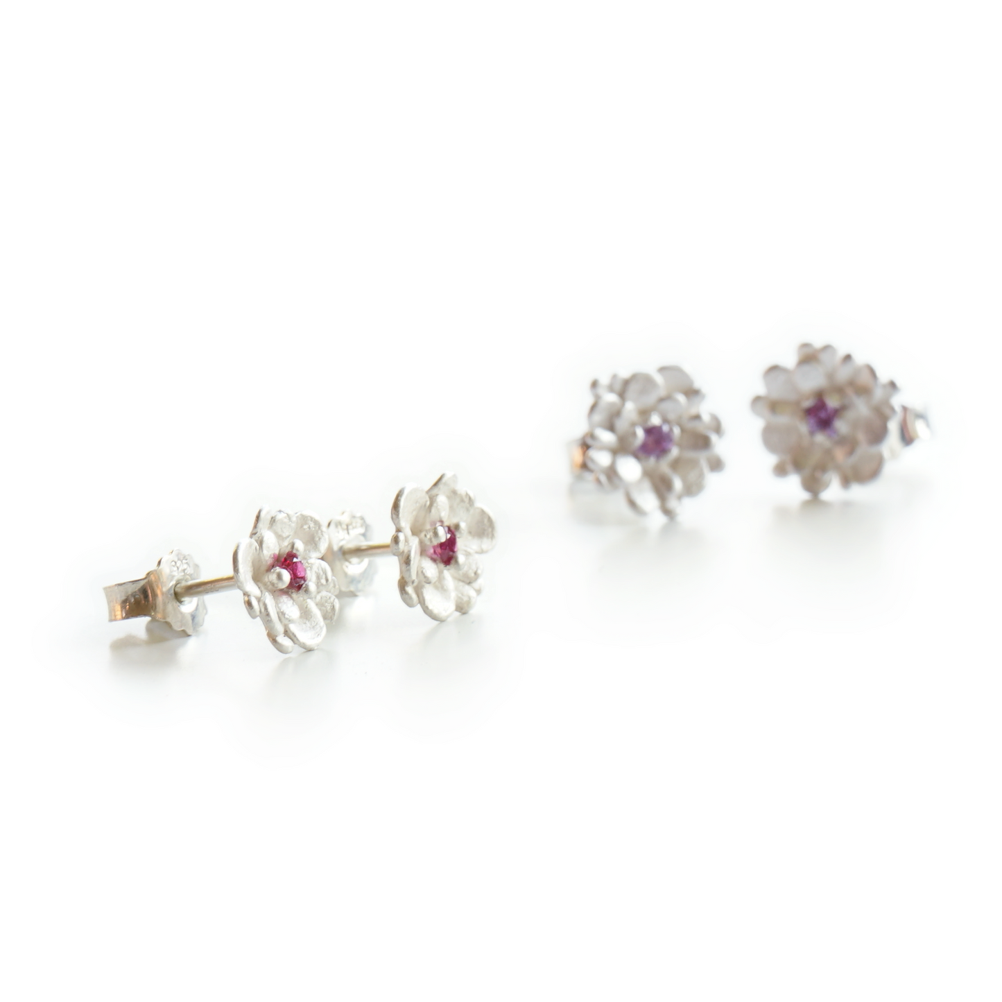 Floral stud earrings in recycled silver with pink sapphire, layered with slightly larger lilac sapphire studs
